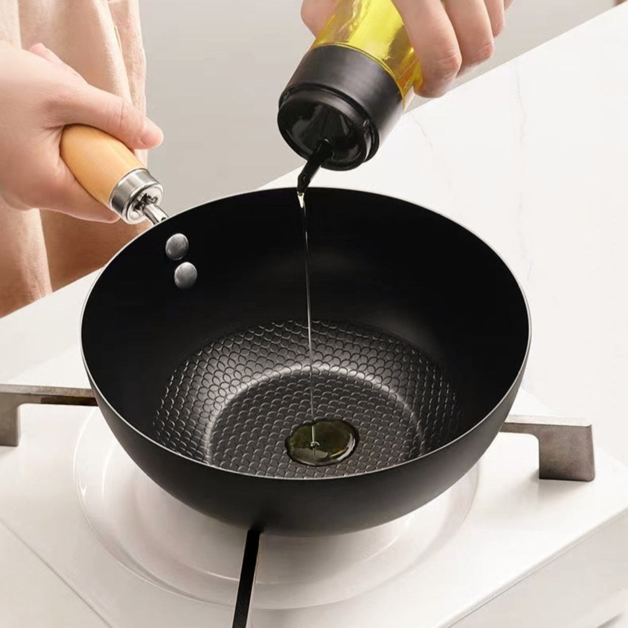 Person pouring oil into a black wok on a stove