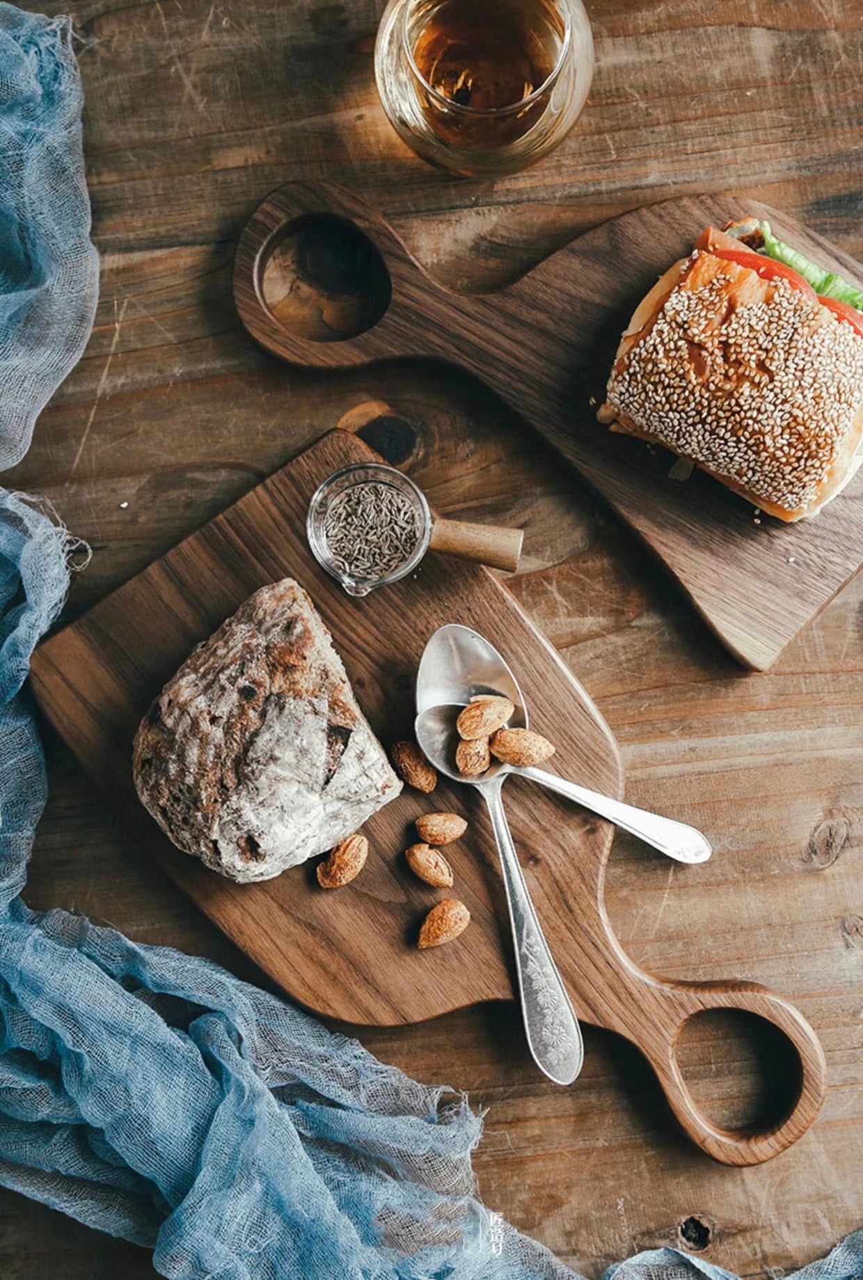 Wooden cutting board with bread, nuts, and a sandwich on a rustic wooden table.