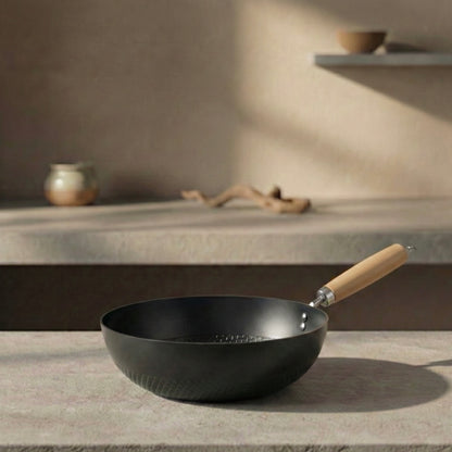 Black wok with a wooden handle on a stone surface